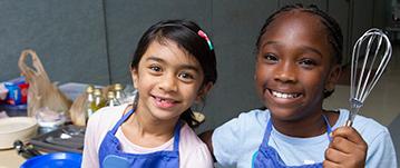 Two little girls smiling in a cooking class.