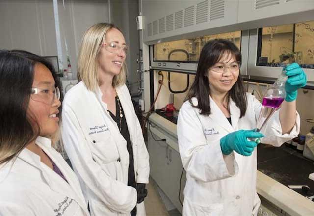 A researcher holding a flask with two colleagues nearby.